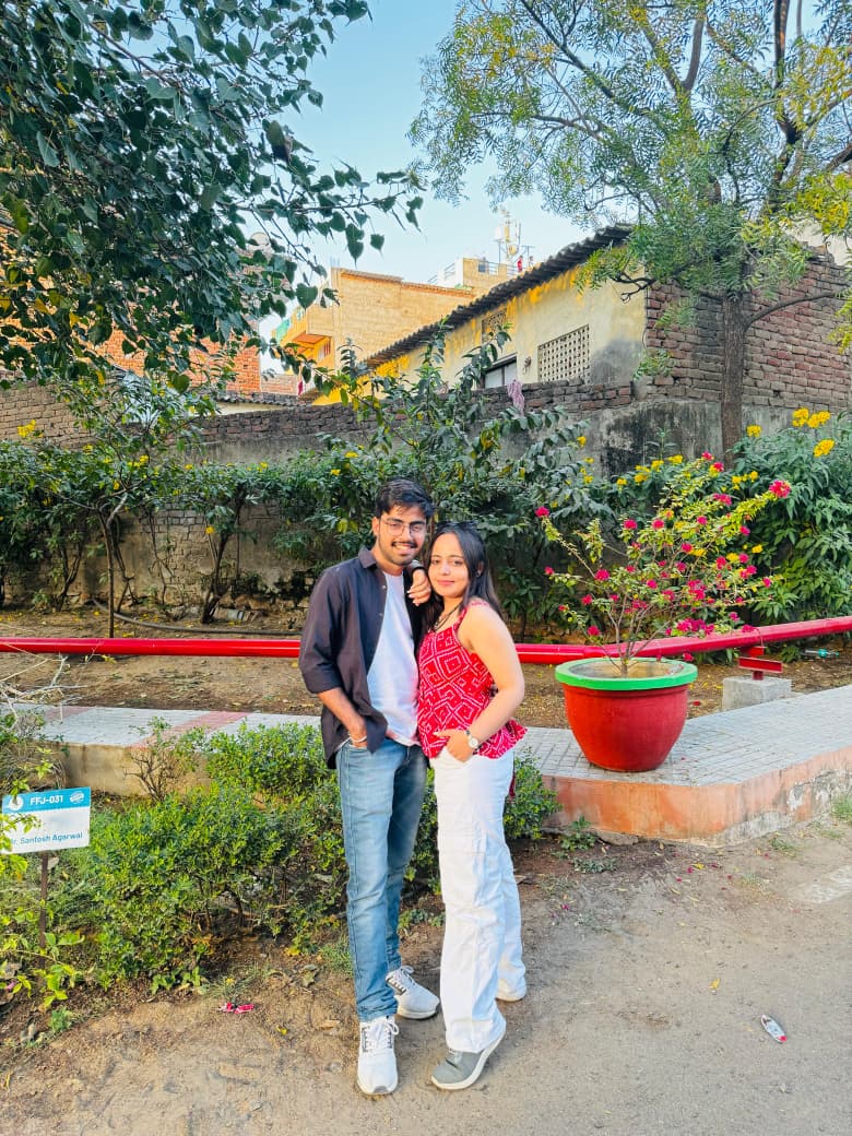 The two of us smiling beside flowers and trees.